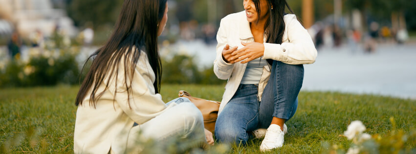 Two women speaking on the grass.